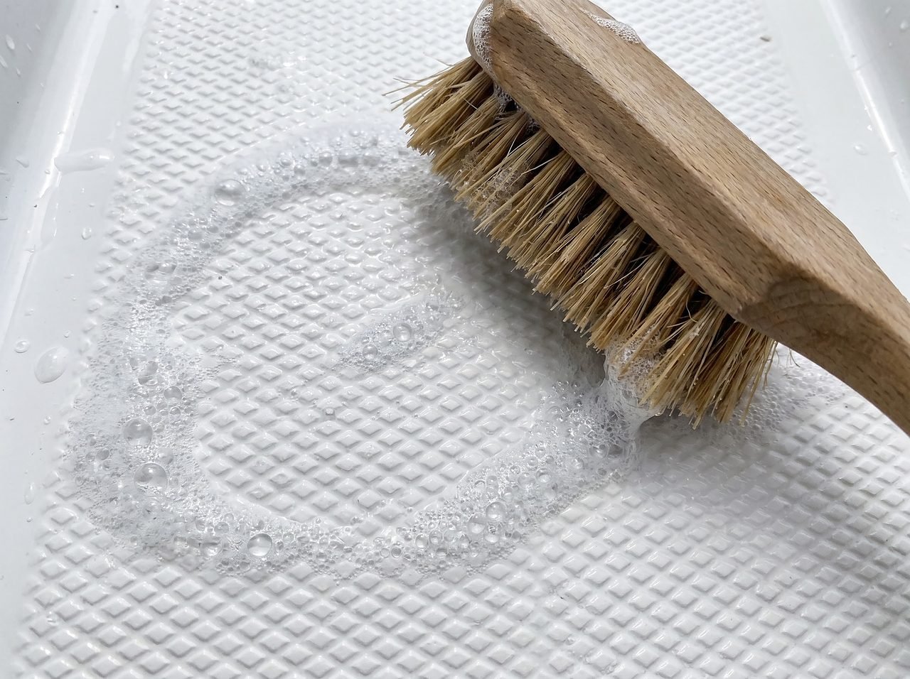 stiff-bristle brush scrubbing textured non-skid deck surface with soapy water