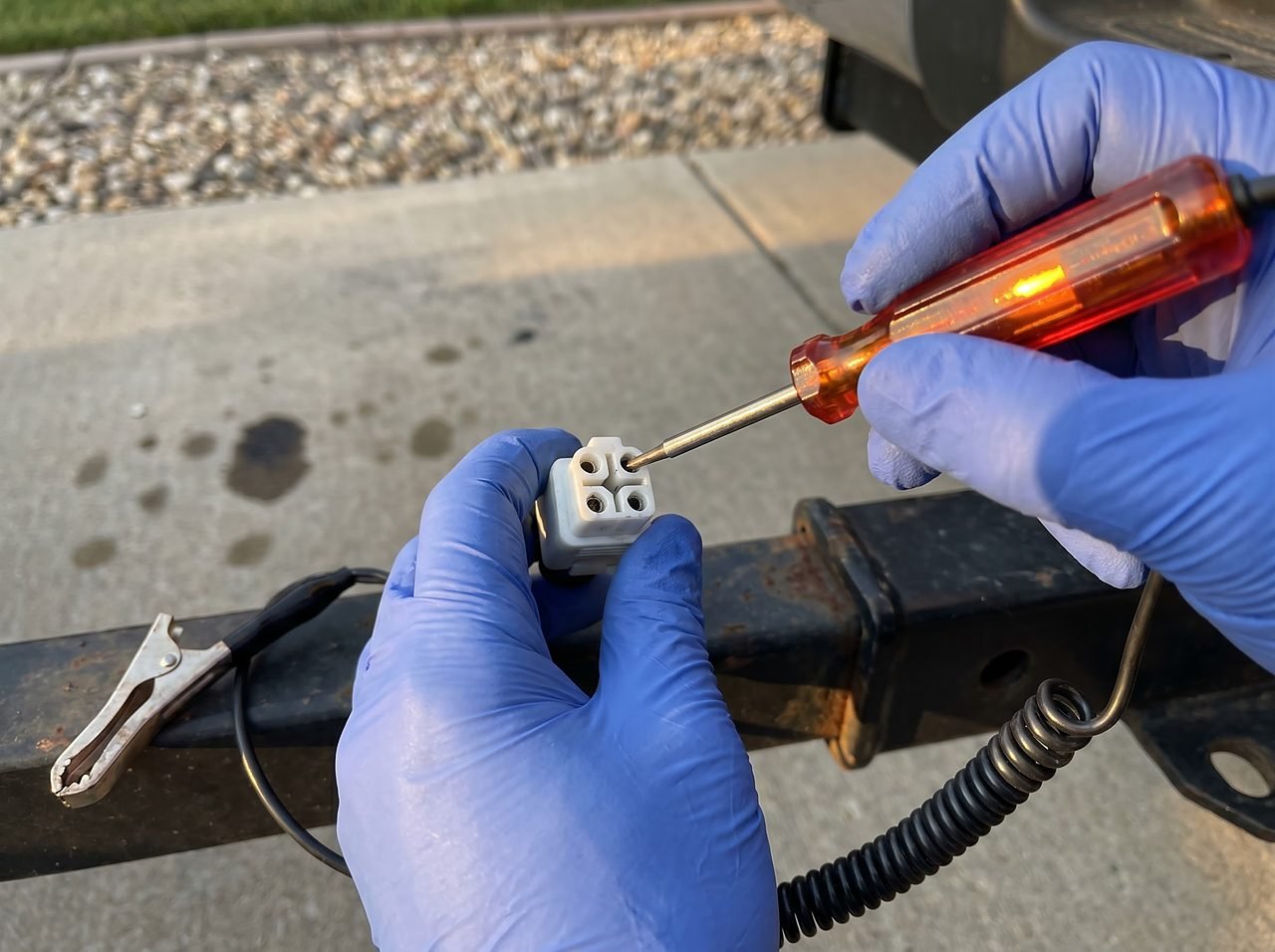circuit tester probe checking a 4-pin trailer connector pin at the hitch