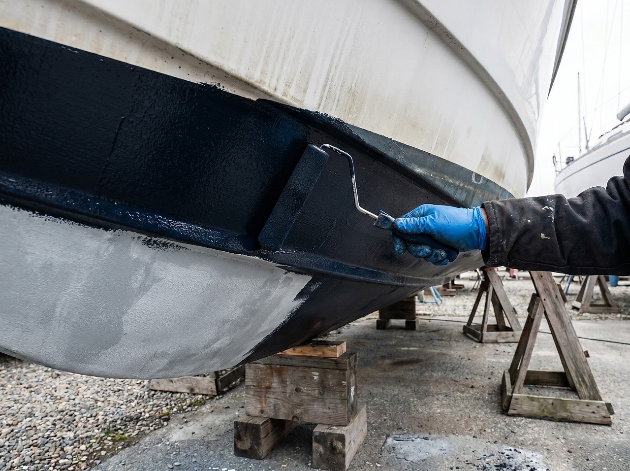antifouling bottom paint being rolled onto a fiberglass hull in a haul-out yard