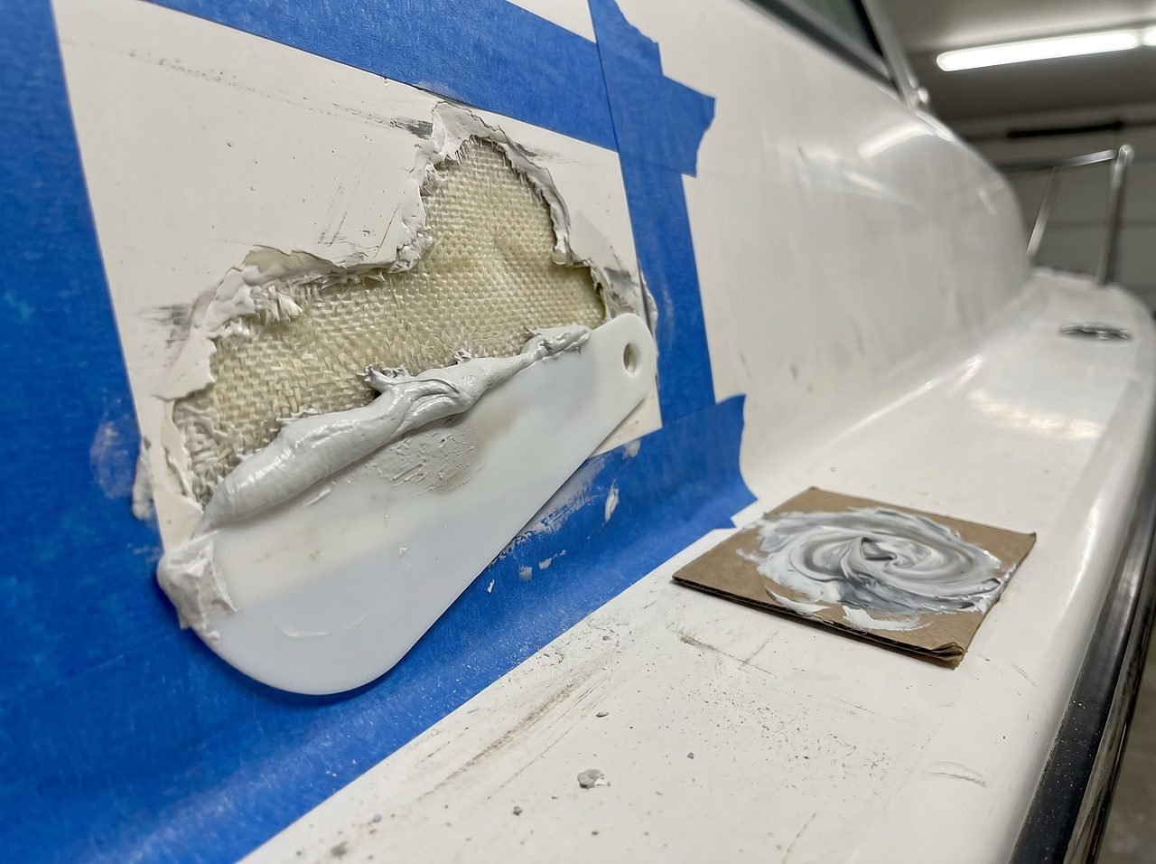 epoxy putty filling a deep gouge that exposes the fiberglass laminate on a boat hull