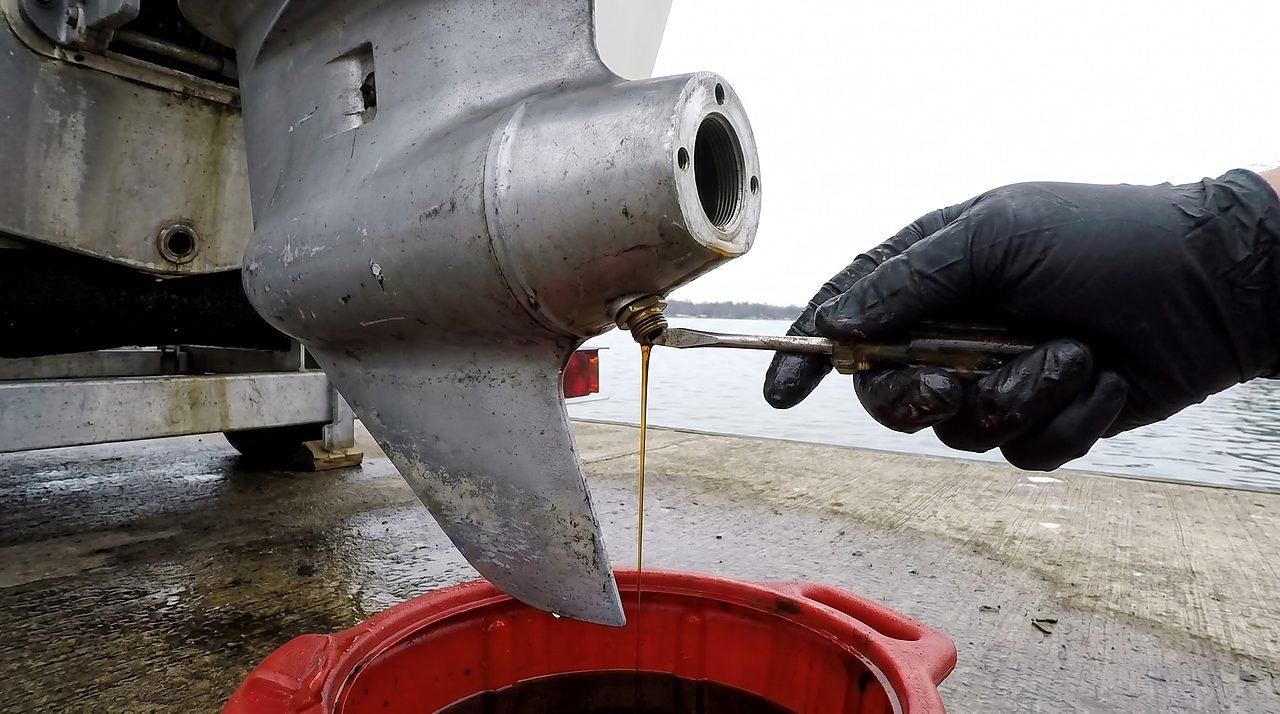 Removing the lower drain screw from an outboard gearcase while amber gear oil flows into a drain pan