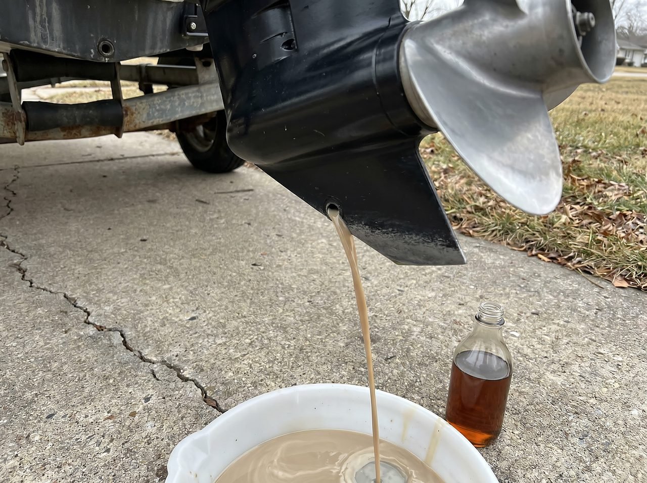 milky lower-unit gear oil draining from an outboard motor during winterization