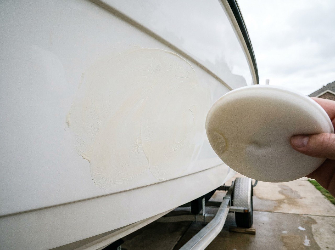 foam applicator pad spreading paste wax in circular motion on white fiberglass boat hull